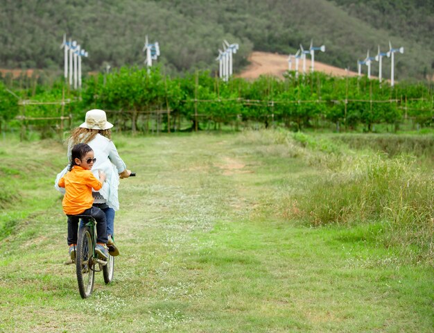 Donna e ragazzo in bicicletta in fattoria con turbine eoliche in background