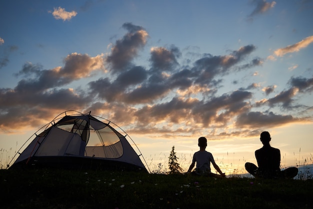 Donna e ragazzo vicino al campeggio al tramonto