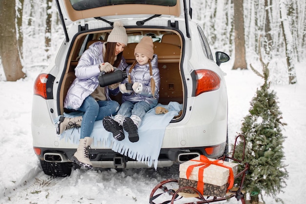 Donna e sua figlia che si siedono nel bagagliaio di un'auto aperta nella foresta d'inverno