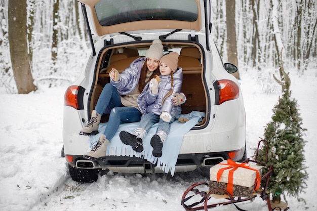 Donna e sua figlia che si siedono nel bagagliaio di un'auto aperta nella foresta d'inverno