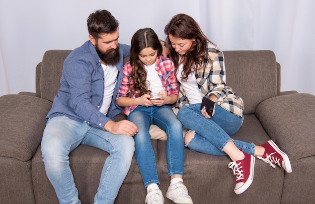 Donna e uomo con bambino seduti insieme sul divano tramite telefono cellulare, famiglia.