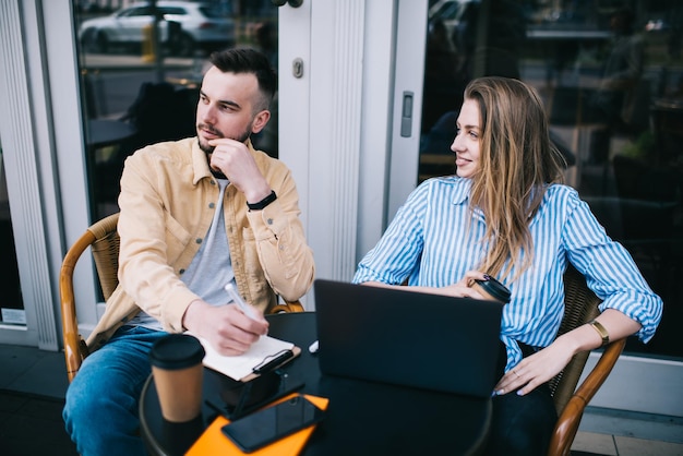 Donna e uomo freelance che scrivono note e navigano sul computer portatile nella caffetteria