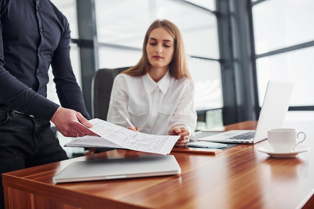 Donna e uomo in abiti formali che lavorano insieme al chiuso in ufficio vicino a un tavolo con documenti.