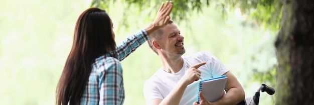 Donna e uomo in sedia a rotelle salutano qualcuno che la gente studia nel parco