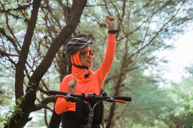 Donna eccitata che alza le mani mentre si pedala sullo sfondo degli alberi