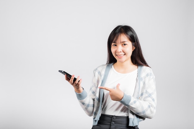 Donna eccitata che celebra la vittoria sì, grandi notizie sullo smartphone che punta il dito sullo sfondo bianco isolato dello studio del telefono cellulare, giovane donna sorridente che ha successo dopo aver ricevuto la promozione