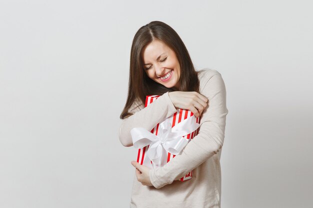 Donna efficace che abbraccia la scatola attuale a strisce rosse con il nastro, arco isolato su fondo bianco. Per la pubblicità. San Valentino, Giornata internazionale della donna, Natale, compleanno, concetto di vacanza.