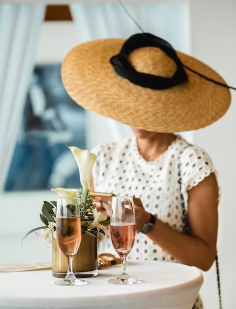 Donna elegante che indossa un cappello di pamela usando il suo telefono ad un evento di lusso.