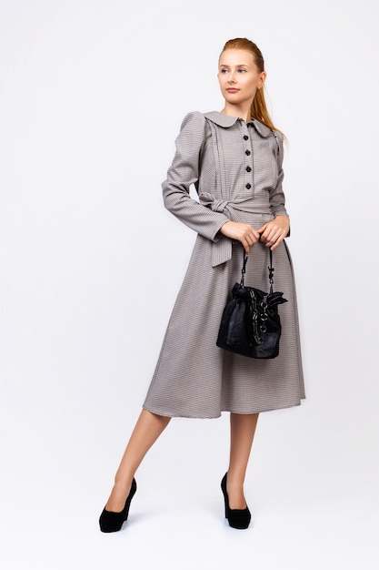 Donna elegante che posa contro un muro bianco, semplice, business, abito grigio