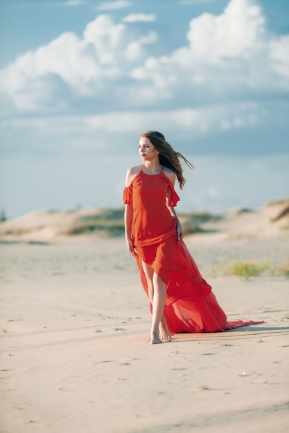 donna elegante che propone sulla spiaggia con il vestito rosso