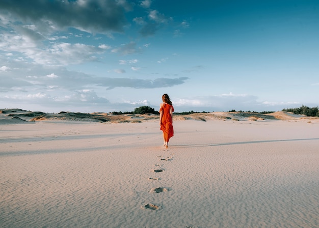 donna elegante che propone sulla spiaggia con il vestito rosso