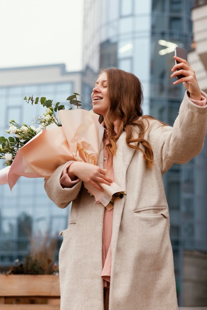 Donna elegante che tiene il mazzo di fiori all'esterno e prendendo selfie