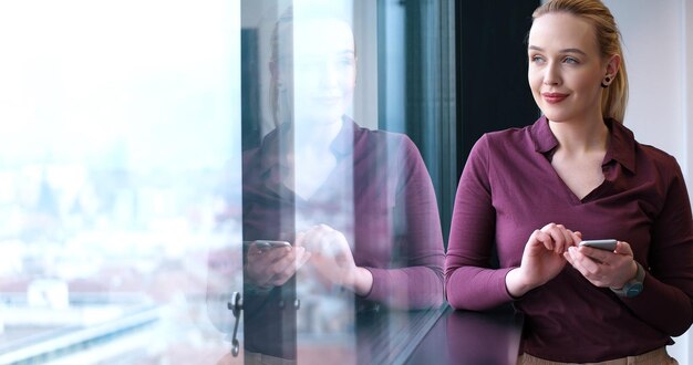 Donna elegante che utilizza il telefono cellulare dalla finestra nell'edificio per uffici