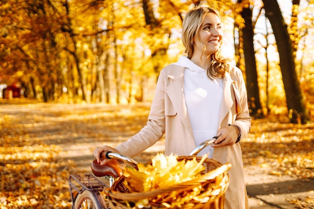 Donna elegante con bicicletta che si gode del tempo autunnale nel parco Donna bella nella foresta autunnale