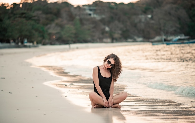 Donna elegante con capelli lunghi in bikini di lusso nero rilassante sulla spiaggia. Vacanze estive.