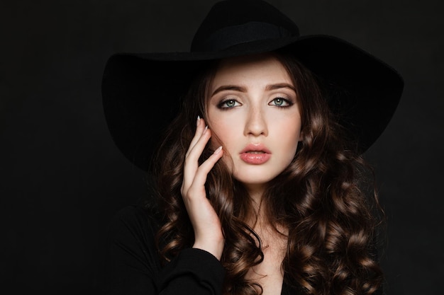 Donna elegante con trucco, capelli ricci e mano curata. Bella modella con cappello nero