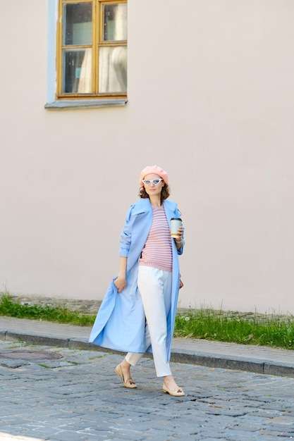 Donna elegante con un impermeabile blu che cammina per strada.