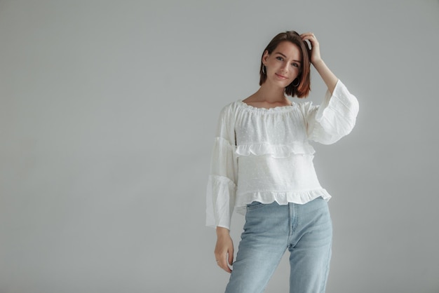 Donna elegante con una camicia bianca e jeans su uno sfondo grigio concetto di grazia e femminilità