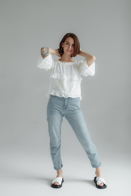 Donna elegante con una camicia bianca e jeans su uno sfondo grigio concetto di grazia e femminilità