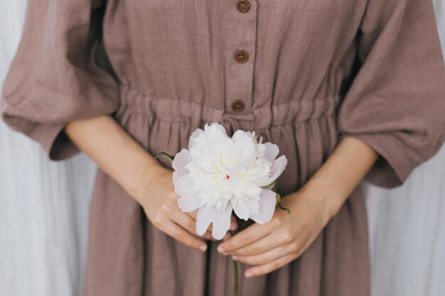 Donna elegante in abito di lino che tiene la peonia nelle mani primo piano Vita lenta Semplice momento estetico
