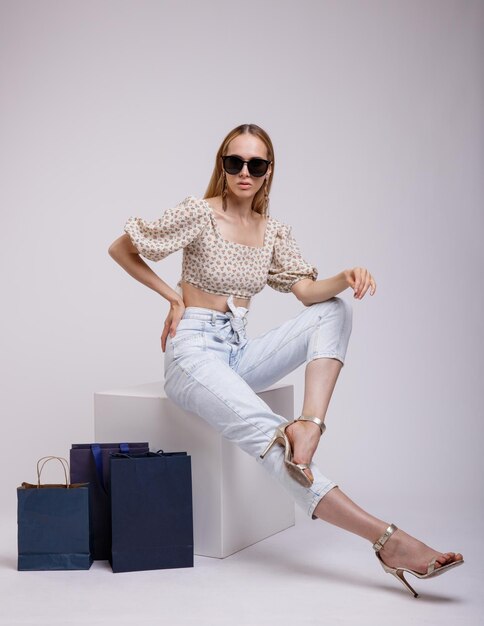 donna elegante in jeans piuttosto blu, top beige, occhiali da sole, borse della spesa su sfondo bianco