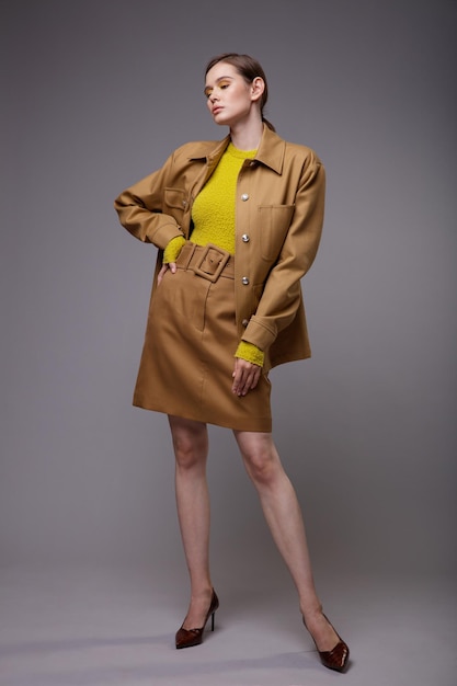 Donna elegante in una giacca di sabbia beige piuttosto marrone gonna maglione giallo senape su sfondo grigio