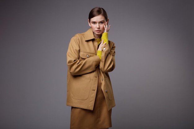 Donna elegante in una giacca di sabbia beige piuttosto marrone gonna maglione giallo senape su sfondo grigio