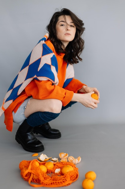 Donna elegante vestita con una giacca lavorata a maglia arancione che posa per una foto in uno studio fotografico su uno sfondo di carta grigia Emozioni luminose pone un concetto moderno