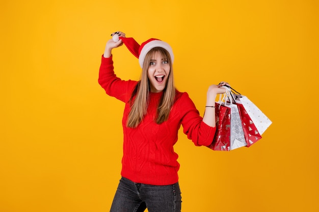 Donna emozionante con i sacchetti della spesa di festa che portano il cappello di Santa e maglione rosso