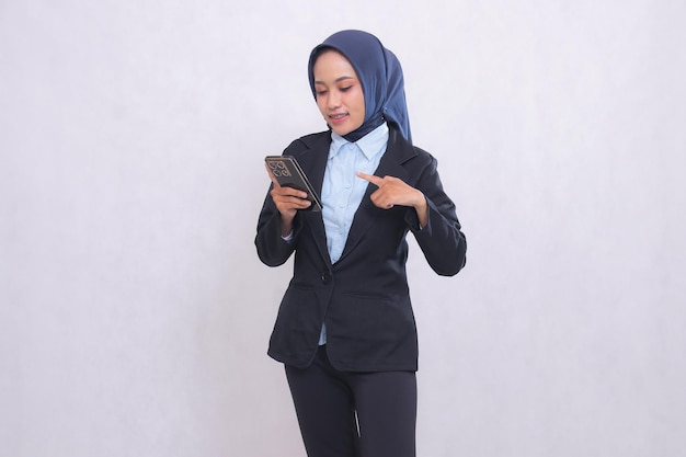 Donna esecutiva di ufficio asiatica che indossa l'hijab in piedi sorridendo guardando e indicando il gadget del cellulare