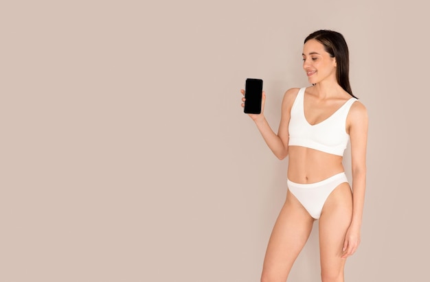 Donna esile in biancheria intima che mostra cellulare con mockup