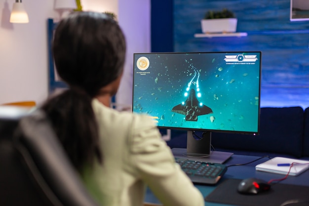 Donna esperta che gioca a un videogioco sparatutto spaziale su un potente pc. La donna competitiva del giocatore informatico che esegue un torneo di videogiochi usa un joystick professionale.