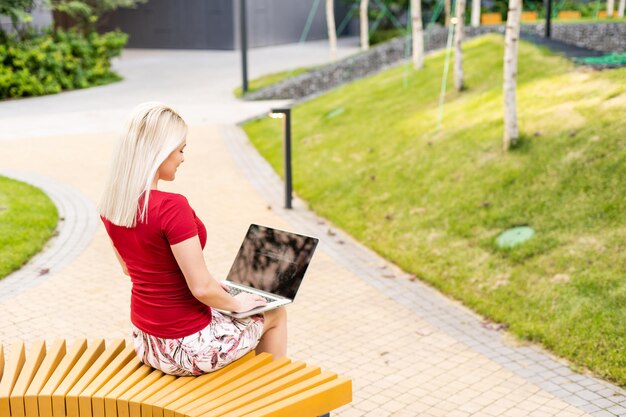 Donna euforica che cerca lavoro con un computer portatile in un parco urbano di estate