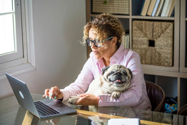 Donna felice a casa innamorata del suo migliore amico pug cane mentre lavora al computer portatile sul desktop