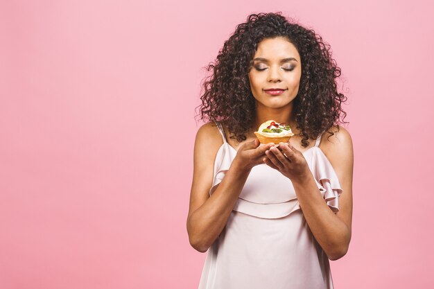 Donna felice afroamericana nera con stile di capelli afro ricci facendo un pasticcio mangiando un dessert fantasia enorme