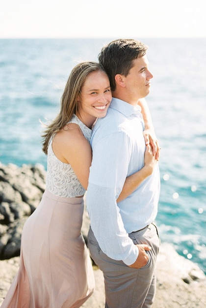 Donna felice che abbraccia un uomo da dietro in piedi su una roccia in riva al mare