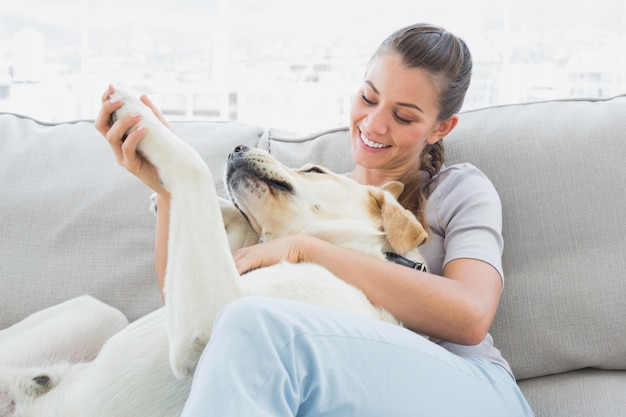 Donna felice che accarezza il suo labrador giallo sul divano