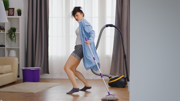 Donna felice che balla mentre pulisce il pavimento della casa con il mop