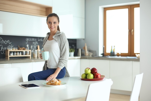 Donna felice che beve il tè in cucina a casa