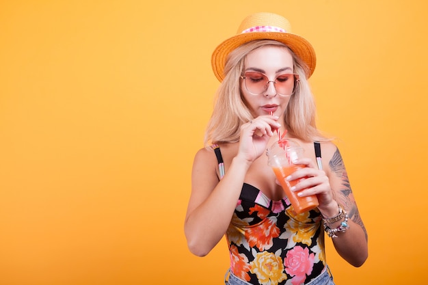 Donna felice che beve succo d'arancia su sfondo giallo in studio