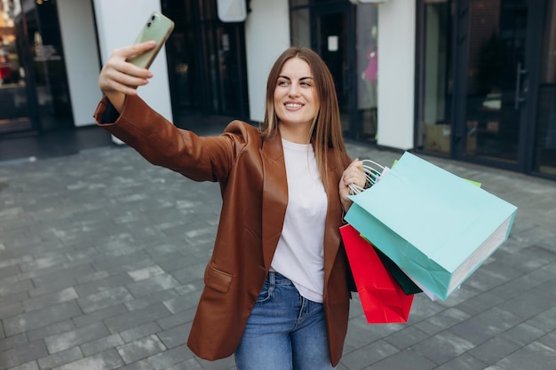 Donna felice che cammina all'aperto tenendo le borse della spesa prendendo selfie con la fotocamera