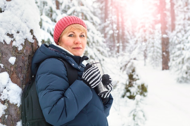 Donna felice che cammina nella foresta di inverno. Una donna di mezza età sta gelando nel parco.