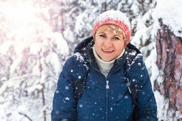 Donna felice che cammina nella foresta invernale. Una donna di mezza età sta congelando nel parco. Bel tempo soleggiato. Lei sorride.