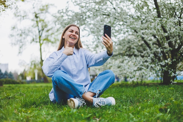 Donna felice che cammina utilizzando lo smartphone in una strada di città Donna d'affari con occhiali da sole utilizza il telefono cellulare all'aperto sotto l'albero in fiore ragazza digitando un messaggio in chat scorrendo la pagina web guarda la fotocamera