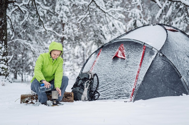 Donna felice che cucina vicino al campo tendato invernale nella foresta di neve