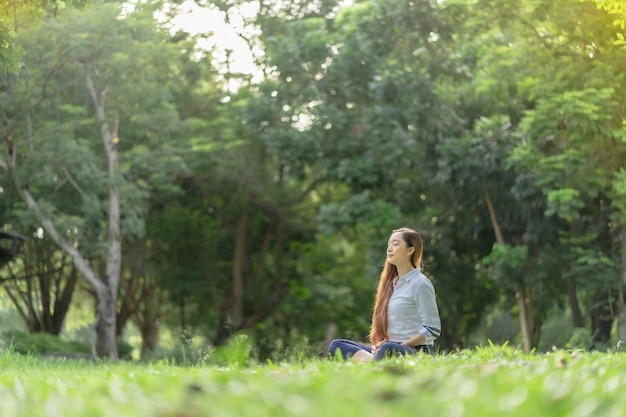 Donna felice che fa meditazione e relax nel parco Meditazione in natura Concetto di stile di vita sano e relax Donna graziosa che pratica la meditazione sull'erba