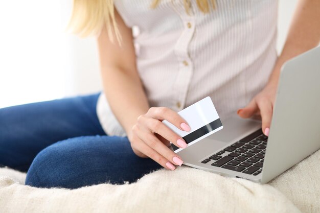 Donna felice che fa shopping online a casa. Primo piano di una mano che tiene una carta di credito accanto a un computer portatile.