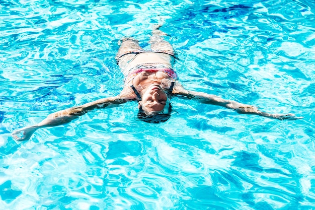 Donna felice che gode in una piscina che galleggia sulla schiena