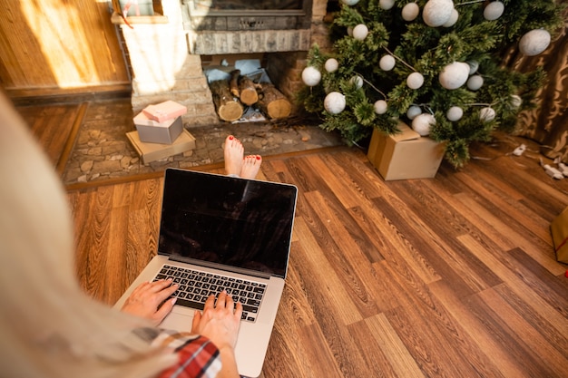 Donna felice che guarda nel computer portatile davanti all'albero di Natale