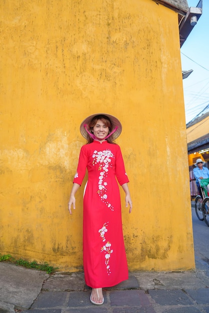 Donna felice che indossa un abito vietnamita Ao Dai e un viaggiatore con cappello che visita la città antica di Hoi An nel punto di riferimento del Vietnam centrale e popolare per le attrazioni turistiche Concetto di viaggio del Vietnam e del sud-est
